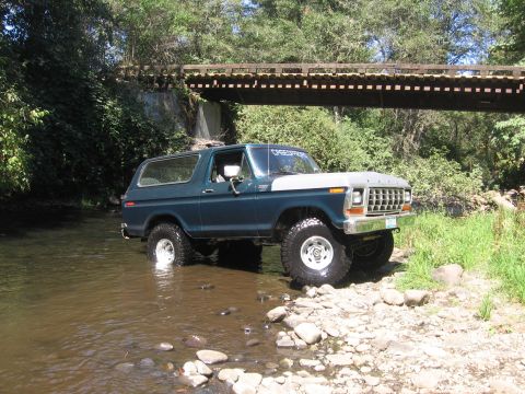 1979 Ford Bronco - A lifted 1978 Ford Bronco navigates a rocky stream bed beneath a wooden bridge.