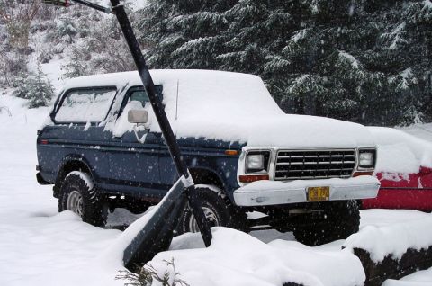 1979 Ford Bronco - A blue SUV is partially covered in snow, with a shovel in the foreground.