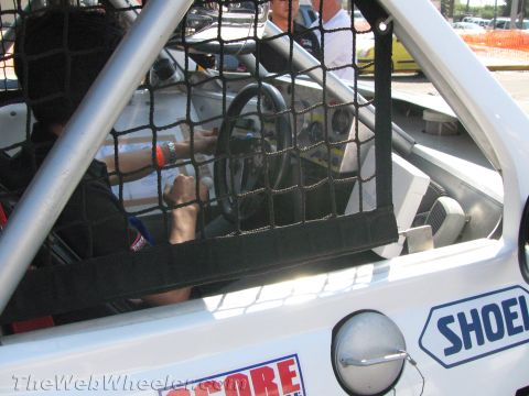 1990 Ford Bronco - View through a window safety net into a white race car cockpit showing the steering wheel and a Shoei door decal.