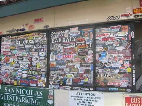 1990 Ford Bronco - Three windows of the San Nicolas Guest Parking building plastered with racing stickers above a hotel attention notice.