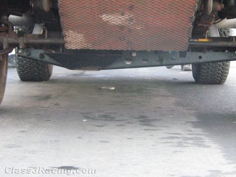 1990 Ford Bronco - under-vehicle view shows the rear suspension, axle, leaf springs and knobby tires of a truck parked on a concrete floor.