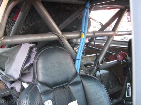 1990 Ford Bronco - interior of an off-road race vehicle shows a roll cage, black vinyl bucket seat and a blue corrugated wiring loom.