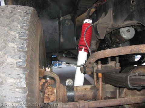 1990 Ford Bronco - close-up of a truck's front suspension shows a mud tire, a red-and-white shock and a rusty leaf spring assembly.