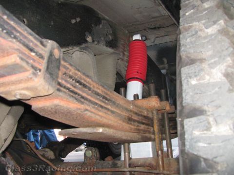 1990 Ford Bronco - undercarriage shot shows rusty leaf springs, a red-and-white shock absorber and a knobby off-road tire.