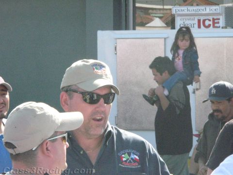 1990 Ford Bronco - man in a ball cap and sunglasses talks in a crowd outdoors beside a packaged-ice vending unit.