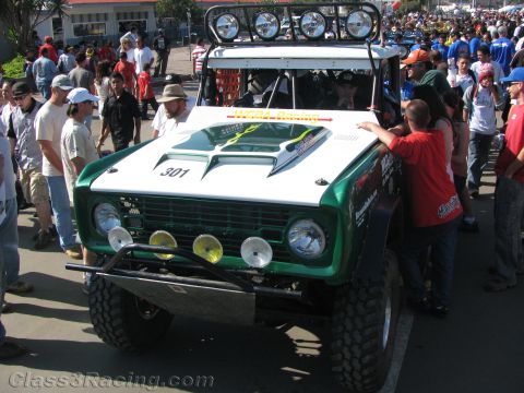 1990 Ford Bronco - Front view of a green-and-white off-road race Bronco numbered 301 with roof light bar amid a large crowd.