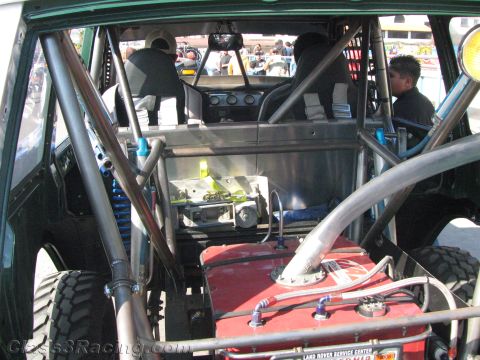 1990 Ford Bronco - Interior of a stripped off-road race vehicle showing roll cage, rear seats, suspension and a red fuel cell.