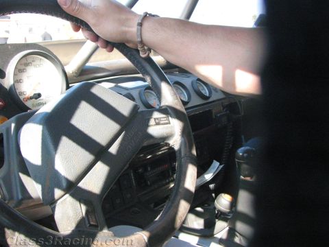 1990 Ford Bronco - hand grips the steering wheel of a Land Rover with a worn airbag pad, round gauges and shifter in sunlight.