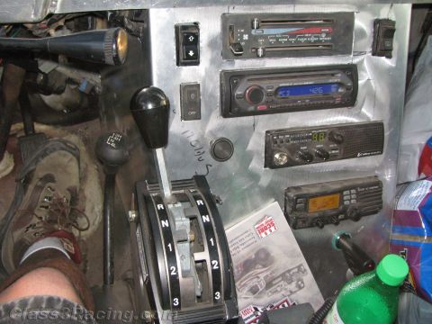 1990 Ford Bronco - Interior of a race vehicle showing a floor-mounted automatic shifter, aftermarket radios and stereo, and a driver's boot resting near the p…