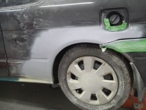 1996 Ford Bronco - Bodywork is underway on the rear passenger side of a car, with primer applied to the fender.