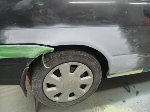 1996 Ford Bronco - Detail of a car's side panel and wheel well, showing primer and masking tape during repair.