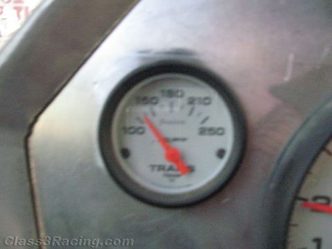 1990 Ford Bronco - Close-up of a round white Auto Meter transmission temperature gauge, its red needle reading near 150 degrees, set in a dark dash panel.