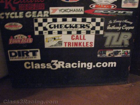 1990 Ford Bronco - Close-up of a dark surface covered in racing decals, prominently featuring a 'Checkers Call Trinkles' sticker and a white 'Class3Racing.com…