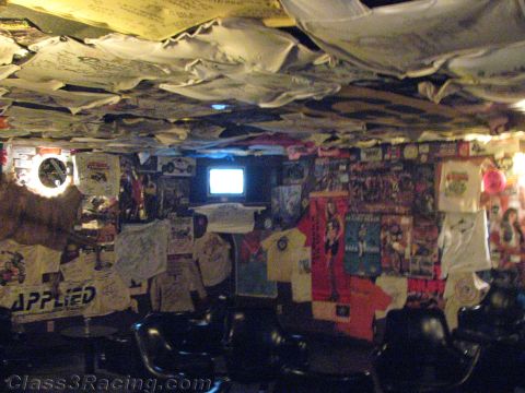 1990 Ford Bronco - dark bar-like room with its ceiling and walls covered in signed shirts, posters and decals, a small lit TV glowing on the far wall above bl…