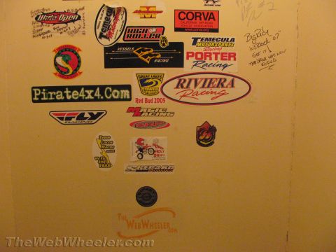 1990 Ford Bronco - yellow wall plastered with racing stickers and decals, including Pirate4x4.com, Riviera Racing, CORVA and a TheWebWheeler.com logo.