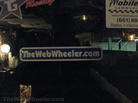 1990 Ford Bronco - dim cluttered interior showing a blue 'TheWebWheeler.com' sign and a white Mobile communications advertisement on the wall.