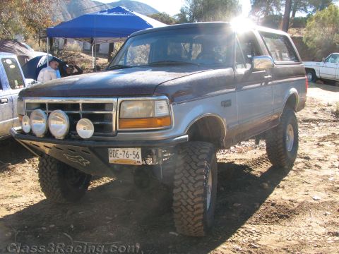 1990 Ford Bronco - lifted blue Ford Bronco fitted with a front light bar and a Mexican license plate sits on a dirt lot beside a blue canopy.