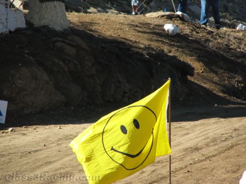 1990 Ford Bronco - bright yellow smiley-face flag flies from a pole in front of a dirt embankment where people stand on the ridge above.