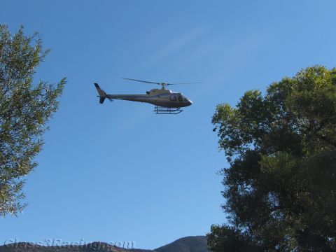1990 Ford Bronco - light-colored helicopter flies against a clear blue sky, framed between the tops of two trees.