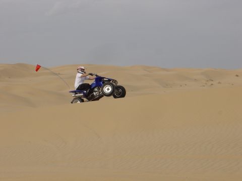 1986 Toyota Hilux - ATV rider catches air while cresting a sand dune under a cloudy sky.