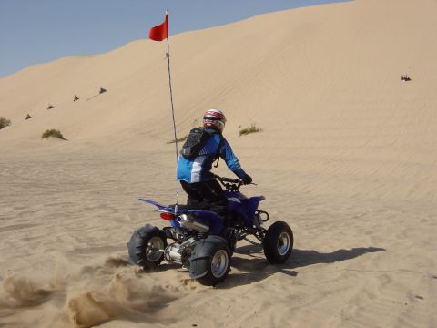 1986 Toyota Hilux - A rider on a blue ATV navigates sand dunes, with other ATVs visible in the distance.