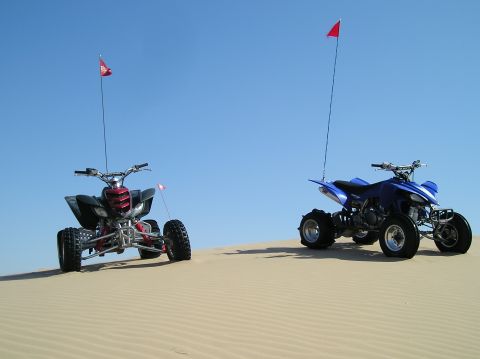 1986 Toyota Hilux - Two quad bikes are parked on sand dunes with red flags flying.