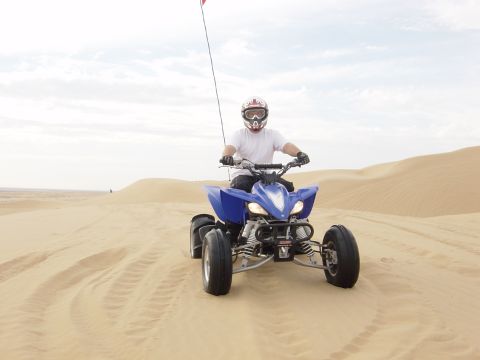 1986 Toyota Hilux - A person rides a blue ATV through sandy terrain under a cloudy sky.