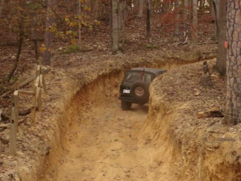 1978 Ford Bronco - A black SUV navigates a challenging dirt trail through a wooded area during autumn.