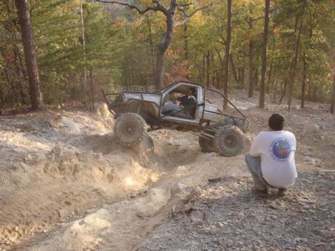 1978 Ford Bronco - A modified off-road vehicle navigates a challenging dirt trail in a wooded area.