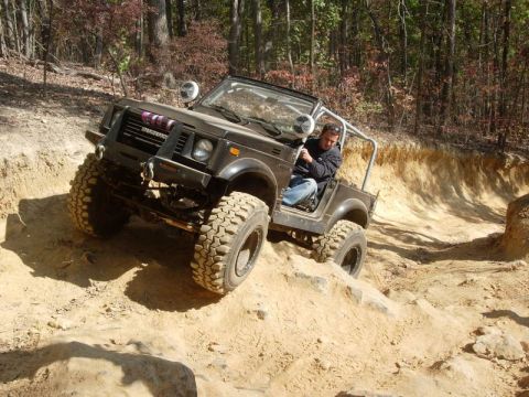 1978 Ford Bronco - A driver navigates a steep, sandy incline on an off-road trail surrounded by trees.