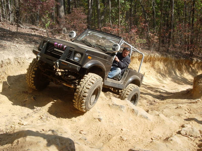 Suzuki Samurai climbing a dirt hill on a wooded trail