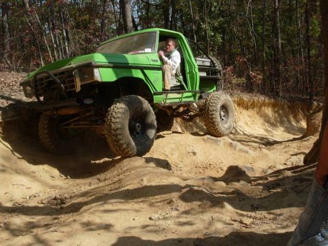 1978 Ford Bronco - Modified green truck navigates a challenging off-road course in a wooded area.