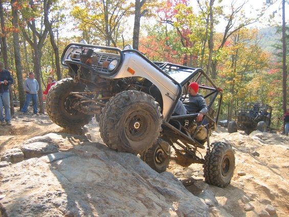 Silver 1978 Ford Bronco modified for off-roading, climbing rocks with a roll cage