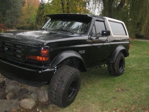 1995 Ford Bronco - This black 1995 Ford Bronco features a white removable top and is shown with oversized tires, giving it a lifted appearance.