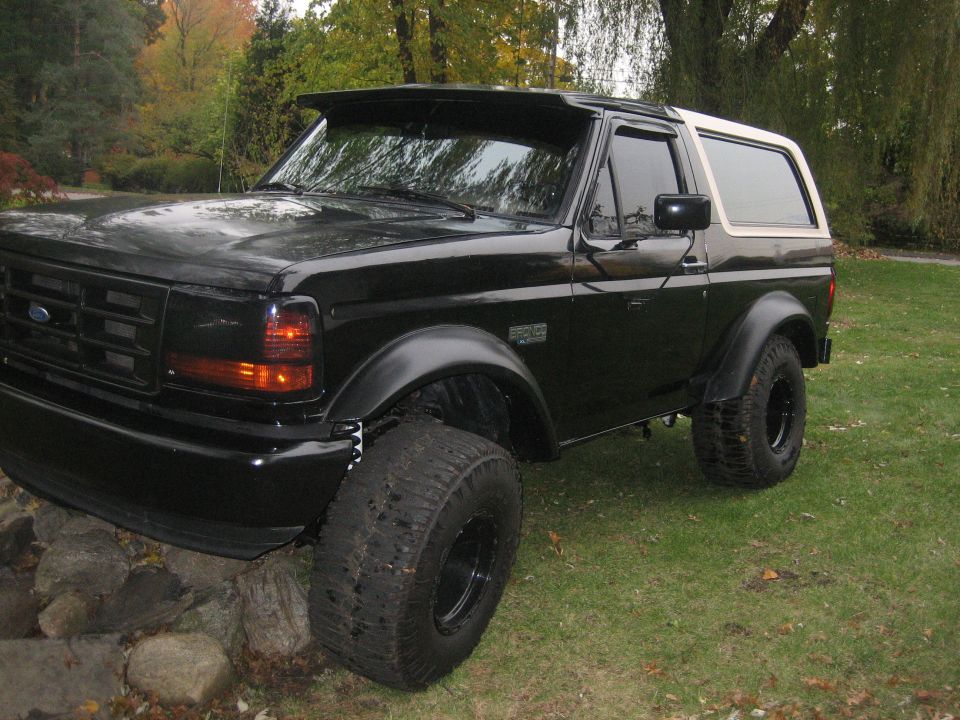 Black 1995 Ford Bronco with large tires and white top parked on rocks and grass