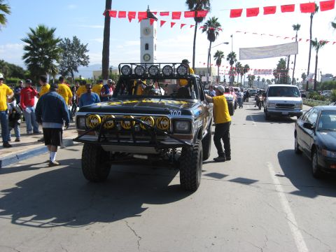 1994 Ford Bronco - Modified 1979 Ford Bronco with off-road lights and roll cage, parked on street with people around.