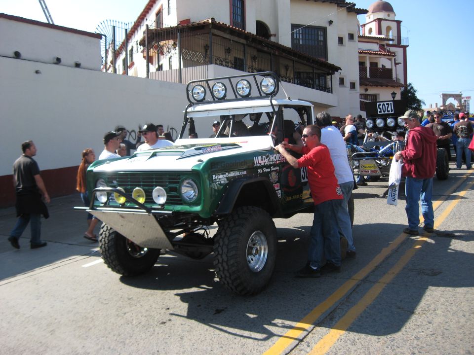 Green off-road SUV with roof lights and large tires, people around it