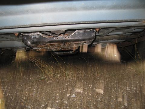 1991 Ford LTD Crown Victoria - The underside of a vehicle is shown, with a rusty undercarriage and grass growing around the tires.