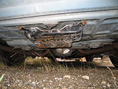 1991 Ford LTD Crown Victoria - Undercarriage detail of a vehicle, focusing on a corroded protective plate and exhaust system.