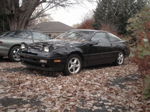1996 Ford Probe - A black Ford Probe sits parked on a driveway covered in fallen leaves, with another car visible behind it.