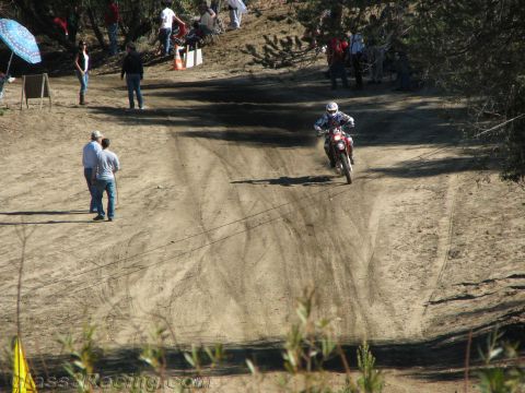 1990 Ford Bronco - helmeted dirt bike rider descends a wide dusty hillside trail as spectators and an umbrella line the off-road course.