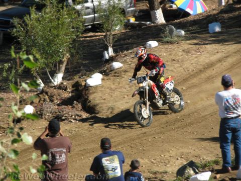 1990 Ford Bronco - dirt bike rider in red gear gets air on a dirt trail as several spectators in the foreground watch and photograph.