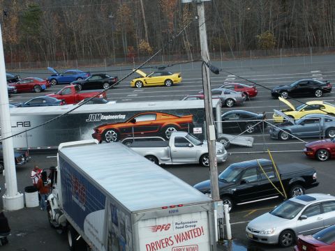 2001 Mercury Grand Marquis - A variety of vehicles are gathered in a parking lot, with a large trailer displaying a car graphic.