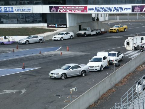 2001 Mercury Grand Marquis - A silver 2001 Ford Mustang coupe is parked on the racetrack, with other vehicles visible in the background.