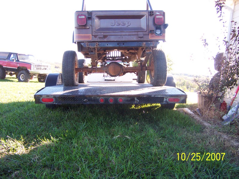 Rear view of a Jeep on a trailer, with a red pickup truck in the background