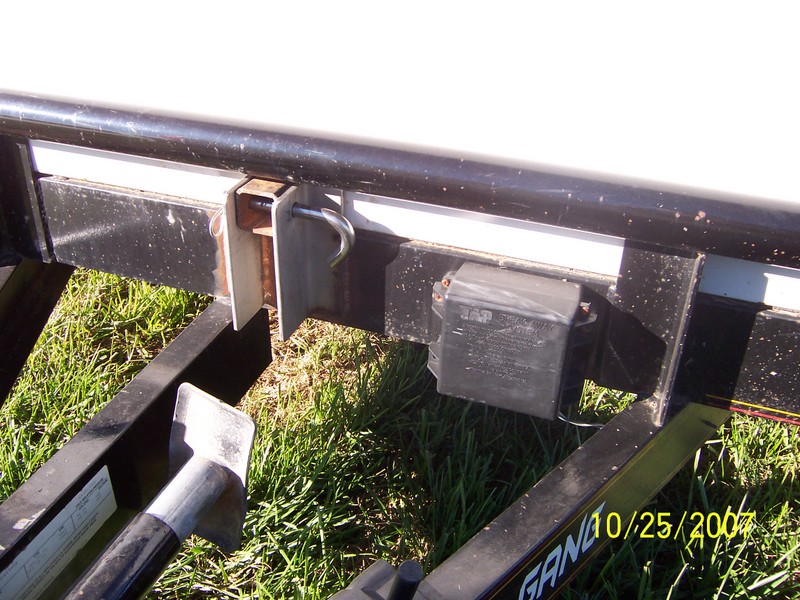 Trailer hitch with a black wiring box and a metal pin. Grass is visible below