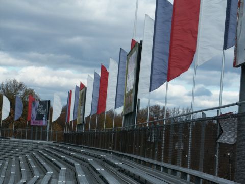 2001 Mercury Grand Marquis - Empty stadium seating is visible under a cloudy sky, with a line of red, white, and blue flags fluttering in the breeze.
