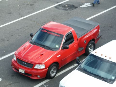 2001 Mercury Grand Marquis - A red Ford F-150 pickup truck is parked next to a white vehicle. The truck has a tonneau cover and a banner on the windshield.