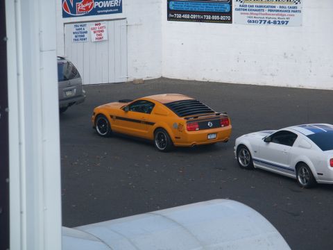 2001 Mercury Grand Marquis - Two Mustangs are parked on asphalt near a building with racing advertisements.