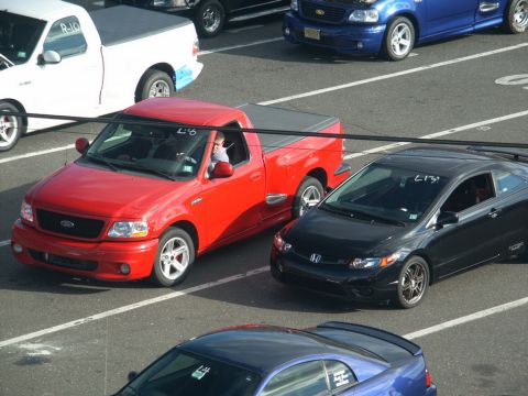 2001 Mercury Grand Marquis - A red Ford F-150 Lightning pickup truck is parked on a track next to a black Honda Civic, with other vehicles visible.